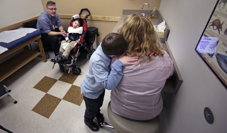 Tyler Volz-Benoit embraces pediatric gastroenterology specialist Dr. Susan Goode during a doctor's appointment with his dad, Eric Volz-Benoit, and brother, Zachary, in Springfield, Mass. Both Tyler and Zachary are affected by complex medical care issues. Zachary is a patient who is helped by a special program funded by the Affordable Care Act, where his health care is overseen by a complex care pediatrician and team of other medical specialists to optimize his care. (AP Photo)