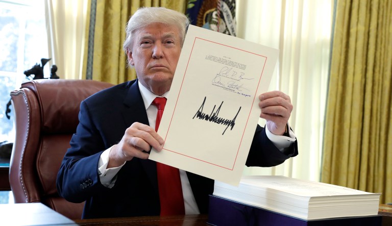 President Trump displays the $1.5 trillion tax overhaul package he signed on Friday in the Oval Office. Trump touted the size of the tax cut, declaring to reporters in the Oval Office before he signed it Friday that 