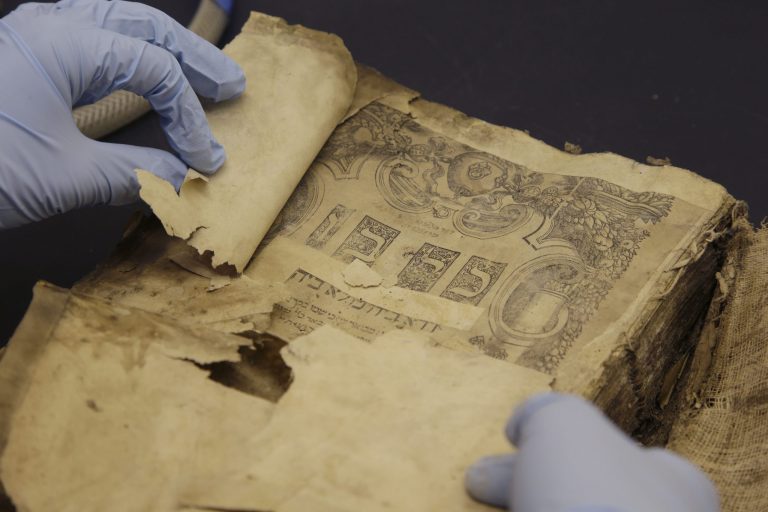 This photo taken Sept. 30, 2013 shows Dina Herbert, a librarian holding the Kol Bo book from the 1540's, that was one of the Iraqi Jewish documents being conserved at the National Archives in College Park, Md. The tattered Torah scroll fragments, Bibles and other religious texts found in a flooded Baghdad basement 10 years ago testify to a once-thriving Jewish population that's all but disappeared from Iraq. Recovered from the Iraqi intelligence headquarters and shipped to the United States for years of painstaking conservation was a literary trove of more than 2,700 books and tens of thousands of documents that are being digitized and put online. A sample of that treasure is being displayed for the first time this fall at the National Archives in Washington.  (AP Photo/Alex Brandon)