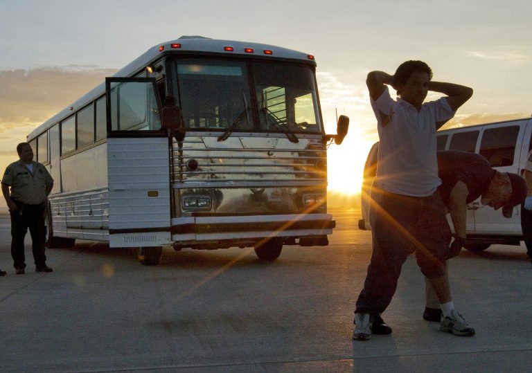 An illegal immigrant from El Salvador is searched on the tarmac at Phoenix-Mesa Gateway Airport as the sun rises prior to boarding an MD-80 aircraft for a repatriation flight. Shackled violent offenders, minors, and women are separated on the flight and are turned over to El Salvador's immigration officers upon arrival. (AP Photo/Matt York)