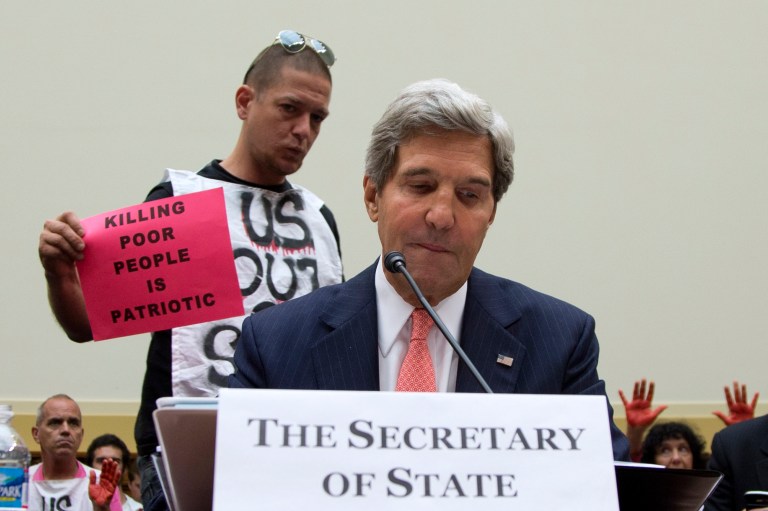 Secretary of State John Kerry pauses as he testifies on Capitol Hill on Wednesday as a protester with CodePink, who are against military action, holds up a sign behind him. (AP/Carolyn Kaster)