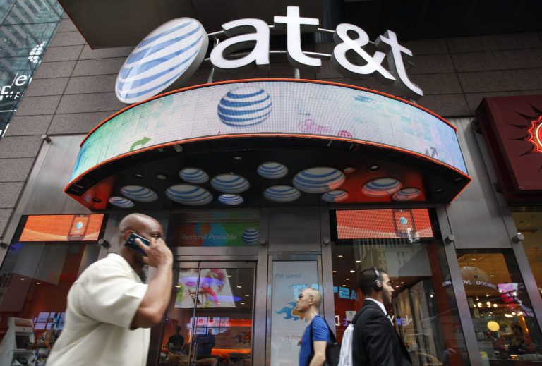 FILE - In this July 11, 2013 photo, a man uses a cell phone as he walks past an AT&T store in New York. AT&T reports quarterly earnings on Tuesday, Jan. 28, 2014. (AP Photo/Mark Lennihan, File)