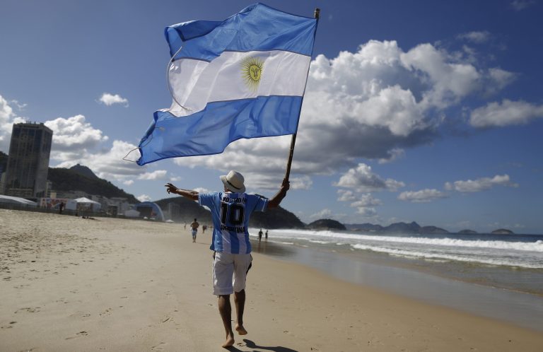 FILE - In this  July 14, 2014, file photo, an Argentina soccer fan waves Argentina's national flag the morning after his team was defeated by Germany at the World Cup final, on Copacabana beach in Rio de Janeiro, Brazil. Local media reports say tens of thousands of Argentine fans have remained in the country after the tournament ended. But the prospect of a large number of foreigners selling handicrafts, juggling at intersections for handouts or relying on government social services for poor Brazilians has officials worried. (AP Photo/Leo Correa, File)