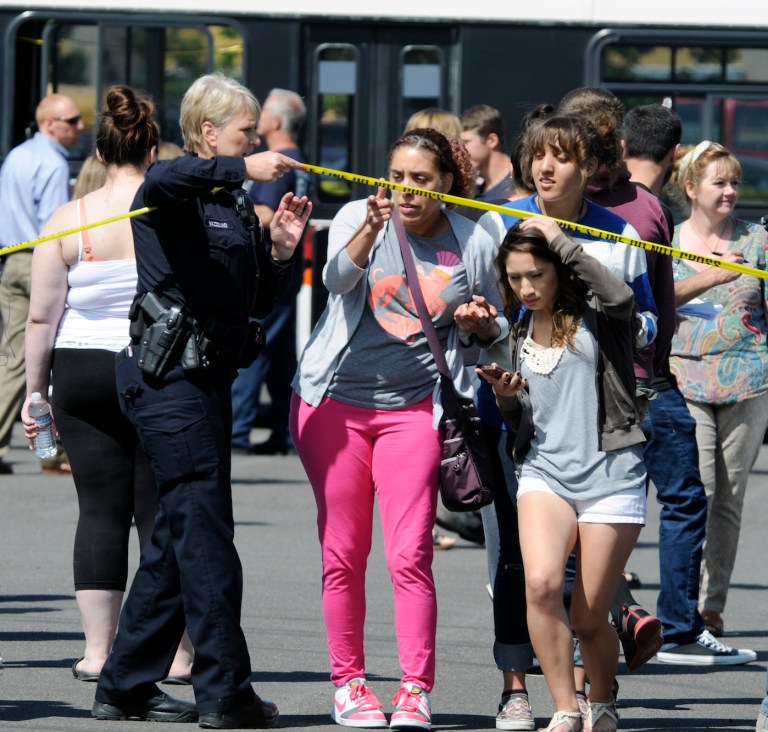FILE - In this Tuesday, June 10, 2014, file photo, a police officer lifts up police tape as students arrive by bus to meet their parents and/or family at the Fred Meyer grocery store parking lot in Wood Village, Ore., after a shooting at Reynolds High School, in nearby Troutdale. Police in Washington state are asking the public to stop tweeting during shootings and manhunts to avoid accidentally telling the bad guys what officers are doing. Two recent incidents led the Washington State Patrol to organize the 