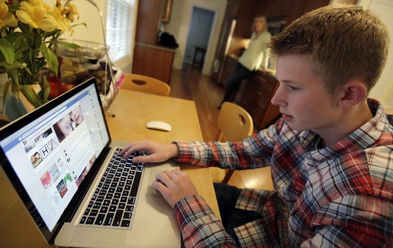 In this Oct. 24, 2013 photo, Mark Risinger, 16, checks his Facebook page on his computer as his mother, Amy Risinger, looks on at their home in Glenview, Ill. (AP Photo)Â 