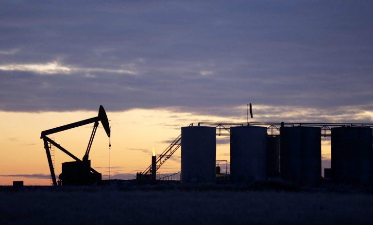 The sun begins to rise behind a pump jack and oil storage tanks near Williston, N.D.