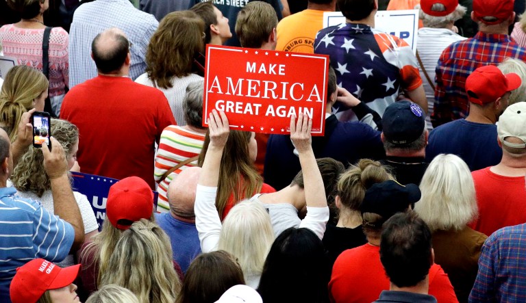 A woman holds up a sign and people listen as then-candidate Donald Trump speaks at a rally on Oct. 1, 2016 in Manheim, Pa.
