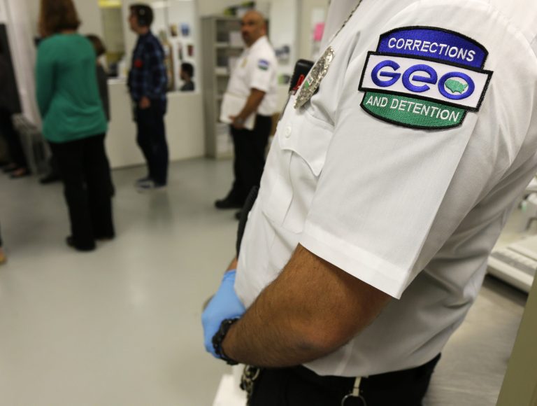 In this photo taken June 21, 2017, a guard with The GEO Group stands in a detainee processing section of the Northwest Detention Center in Tacoma, Wash., during a media tour of the facility. The state of Washington sued GEO on Wednesday, Sept. 20, 2017, claiming thousands of detainees were paid $1 per day for the work they performed but should have received the state's much higher minimum wage.