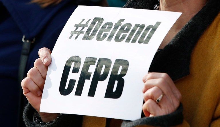 Sally Greenberg, with the National Consumers League, right, holds a sign that says "Defend CFPB" outside of the Consumer Financial Protection Bureau in Washington, Monday, Nov. 27, 2017, during a news conference with consumer groups that oppose Mick Mulvaney being named acting director for the bureau.