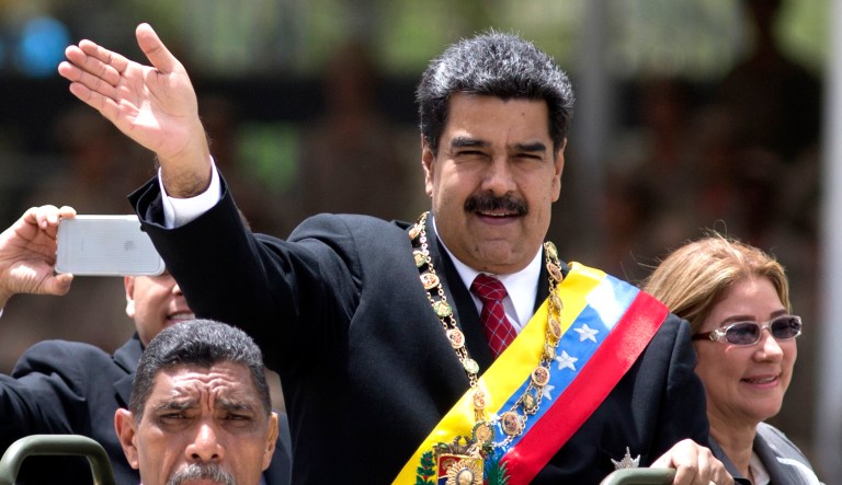 Venezuela's President Nicolas Maduro (center) waves alongside first lady Cilia Flores (right) as they ride in an open vehicle during a military parade.