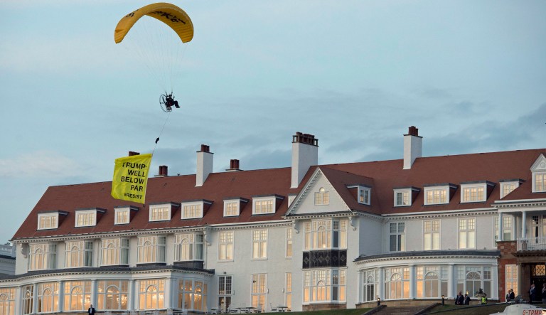 In this Friday, July 13, 2018 photo, a Greenpeace protester flying a microlight passes over President Trump's resort in Turnberry, South Ayrshire, Scotland with a banner reading "Trump: Well Below Par", shortly after the US President arrived at the hotel. Scottish police said the protester breached a no-fly zone over Turnberry hotel and committed a criminal offense.