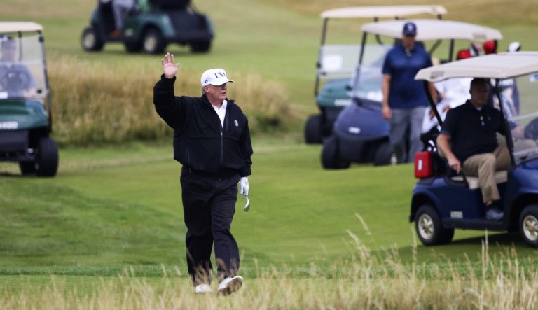 U.S. President Donald Trump waves to protesters while playing golf at Turnberry golf club, in Turnberry,  Scotland, Saturday, July 14, 2018.