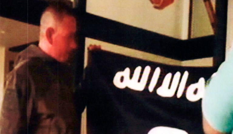 In this July 8, 2017 file image taken from FBI video and provided by the U.S. Attorney's Office in Hawaii on July 13, 2017, Army Sgt. 1st Class Ikaika Kang holds an Islamic State group flag after allegedly pledging allegiance to the terror group at a house in Honolulu. Kang is set to plead guilty Wednesday, Aug. 29, 2018, as charged in an indictment last year, defense attorney Birney Bervar said. He is agreeing to a 25-year sentence for charges that could have put him in prison for life.