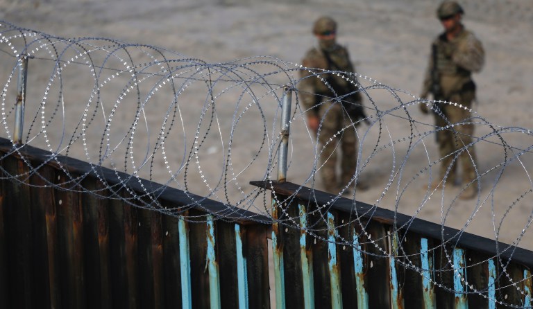 U.S. Border Patrol agents stand on the U.S. side of the border, seen through the concertina wire from the Mexican side where the border meets the Pacific Ocean, Friday, Nov. 16, 2018.