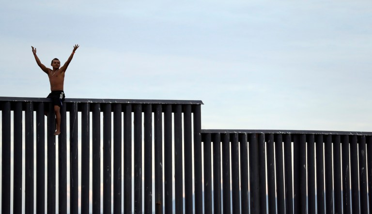 A man from Honduras jokes as he briefly straddles the border wall separating Tijuana, Mexico and San Diego, before climbing back down on the Mexican side, Wednesday, Nov. 21, 2018, seen from San Diego. Migrants traveling by caravan from Central America continue to arrive in Tijuana, where the border has been fortified by razor wire in many sections by U.S. authorities. 