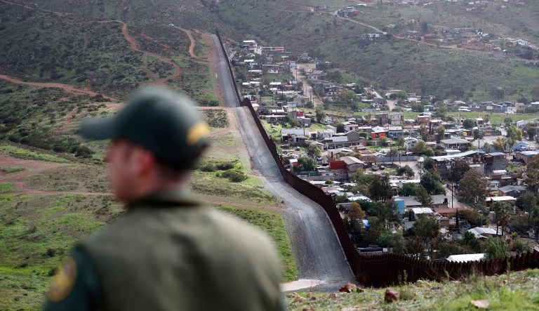 An officer on the American side of the U.S.-Mexico border walks near a wall.