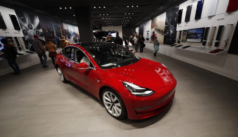 In this Saturday, Feb. 9, 2019 photograph, buyers look over a Model 3 in a Tesla store in Cherry Creek Mall in Denver. 