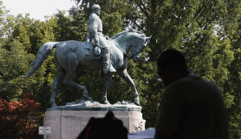 In this Aug. 6, 2018 photo, a visitor eats lunch in front of a statue of Robert E. Lee that is surrounded by fencing and a No Trespassing sign in Charlottesville, Va. A Virginia judge has ruled that Charlottesvilleâs Confederate statues are war monuments protected by state law. 