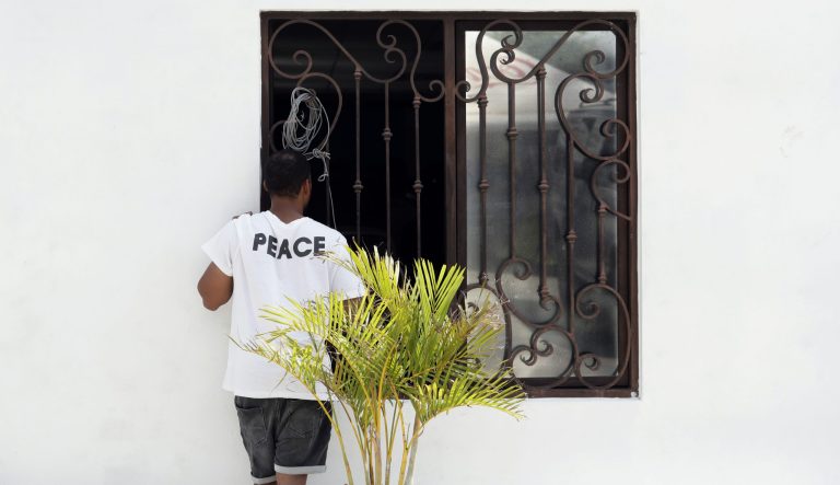 In this Wednesday, May 1, 2019, photo, an asylum seeker stands at a church window as he waits at a shelter in Reynosa, Mexico. The turning away of most asylum seekers by U.S. officers standing at the bridge connecting Reynosa, Mexico, to McAllen, Texas, has created more business for the criminal networks known to control most aspects of life here. 