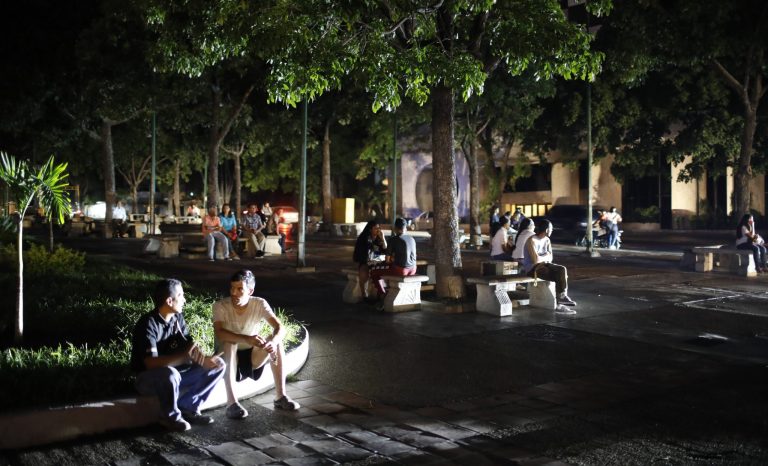 People seat on a square during a blackout in Caracas, Venezuela, Monday, July 22, 2019. The lights went out across much of Venezuela Monday, reviving fears of the blackouts that plunged the country into chaos a few months ago as the government once again accused opponents of sabotaging the nation's hydroelectric power system. 