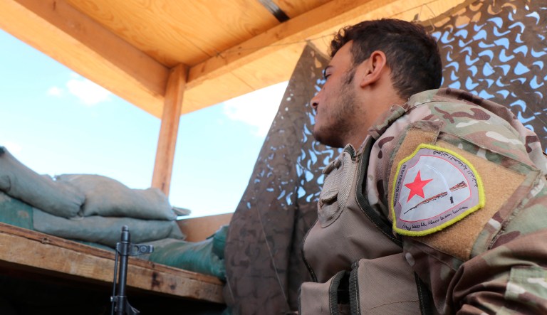 A fighter from the Syrian Democratic Forces, SDF, stands guard inside a post where U.S. troops were based, in Tal Abyad town, at the Syrian-Turkish border, Syria, Monday, Oct. 7, 2019. The SDF, a U.S.-backed Kurdish-led force accused Washington Monday of failing to abide by its commitments by withdrawing from northeast Syria ahead of a Turkish invasion that the Kurds say will overturn five years of achievements in the battle against the Islamic State group. 