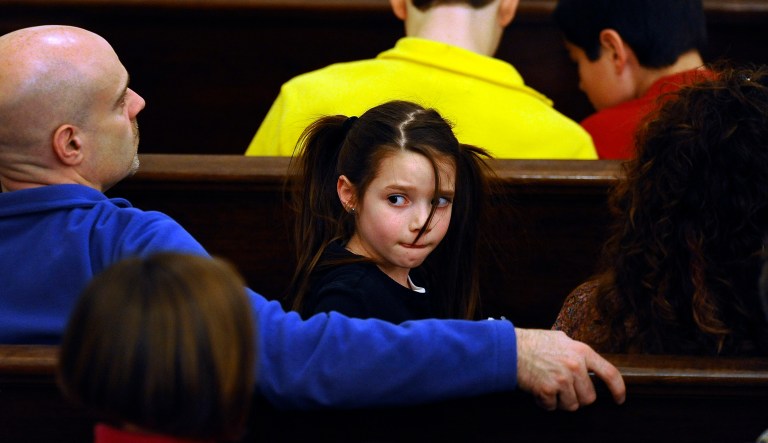 A girl sits with her family in a pew during a sermon at a church.