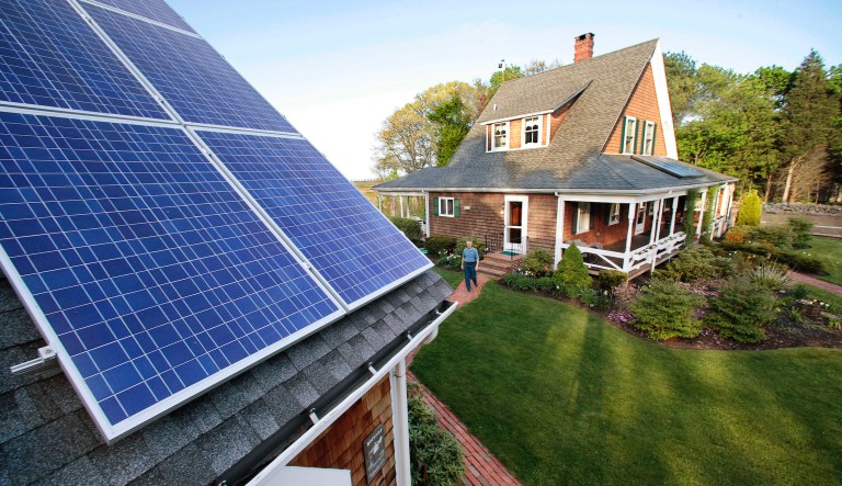 In this May 8, 2009, file photo, Len Bicknell walks from his house to his garage where his solar energy panels are mounted on the roof in Marshfield, Mass.