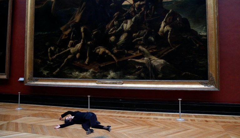 An activist lies on the floor inside the Louvre museum, as he stages a protest trying to call attention to migration driven by climate change, and notably to criticize activities of French oil giant Total, a prominent sponsor of Louvre activities, in Paris, Monday, March 12, 2018.