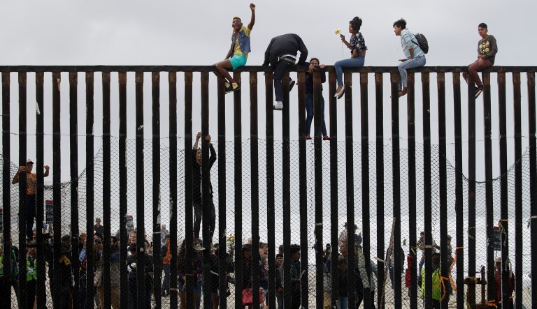 Central American migrants sit on top of the border wall on the beach in San Diego during a gathering of migrants living on both sides of the border. 