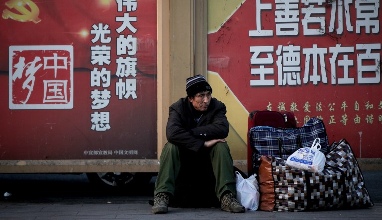A migrant worker sits next to his belonging against a wall displaying a Chinese government propaganda message at the Beijing railway station in Beijing, Monday, Jan. 21, 2019. China's economic growth hit a three-decade low in 2018, adding to pressure on Beijing to beef up stimulus measures and settle a tariff war with Washington.