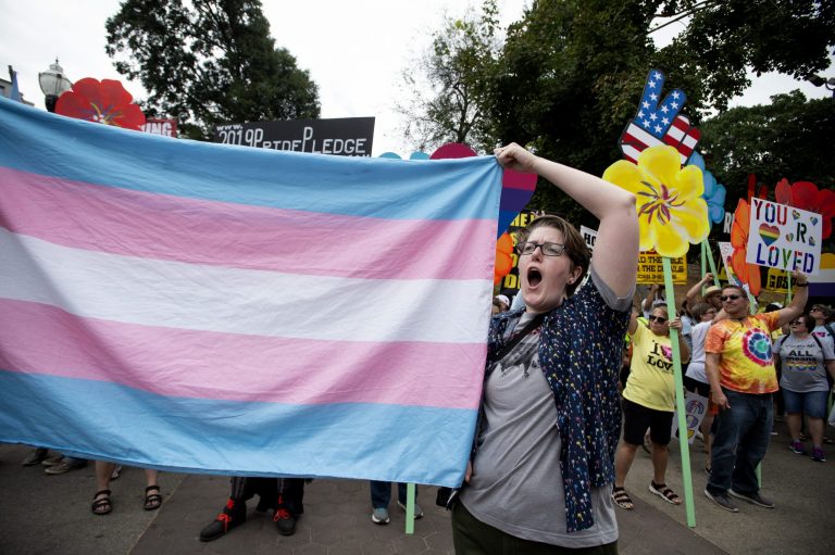 A supporter for the transgender community holds a trans flag in front of counter-protesters to protect attendees from their insults and obscenities at the city's Gay Pride Festival in Atlanta on Saturday, Oct. 12, 2019. Transgender women who were born male must register for the military draft with the Selective Service, while transgender men who were born female donât have to sign up, according to the Selective Service. (AP Photo/Robin Rayne)