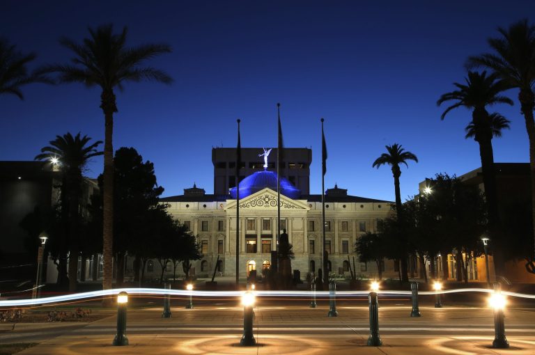 The blur of car lights zip past the Arizona Capitol as the dome is illuminated in blue, along with other buildings and structures around the state on Wednesday, April 15, 2020, in Phoenix. (AP Photo/Ross D. Franklin)