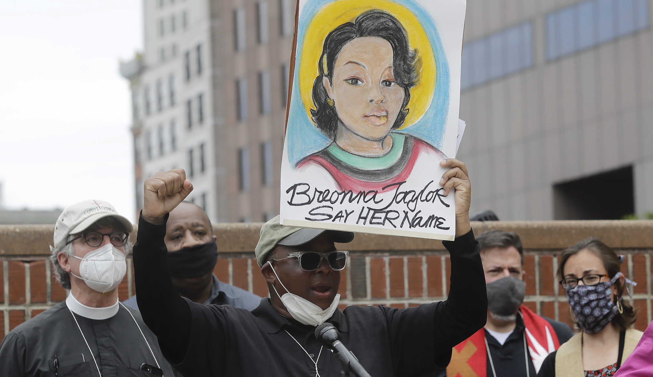 Kevin Peterson, the founder and executive director of the New Democracy Coalition, center, displays a placard showing Breonna Taylor as he addresses a rally.