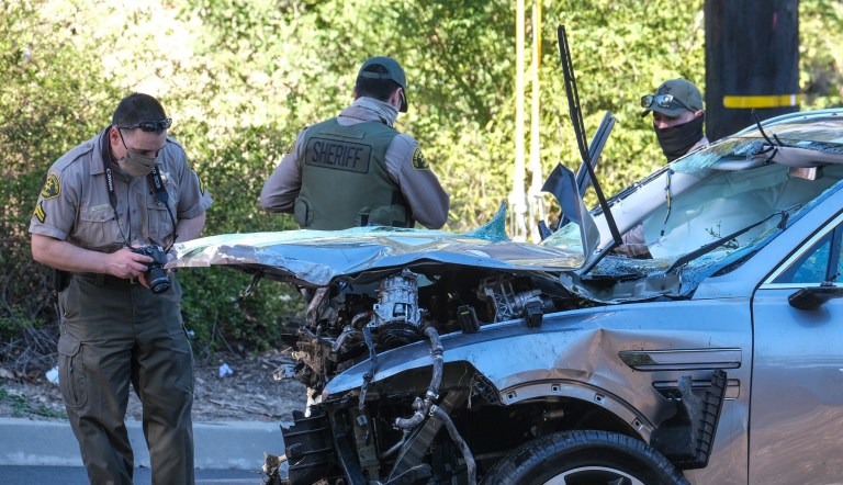 Law enforcement officers look over a damaged vehicle following a rollover accident involving golfer Tiger Woods, Tuesday, Feb. 23, 2021, in the Rancho Palos Verdes suburb of Los Angeles. Woods suffered leg injuries in the one-car accident and was undergoing surgery, authorities and his manager said.