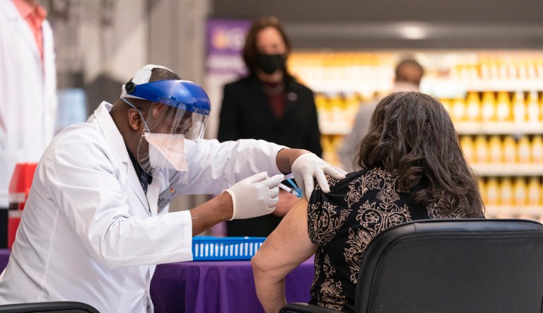 Vice President Kamala Harris, background, watches as physician Linval Matthews, left, administers a Moderna COVID-19 vaccine to Brenda Thompson, right, at a Giant Foods grocery store, Thursday, Feb. 25, 2021, in Washington.