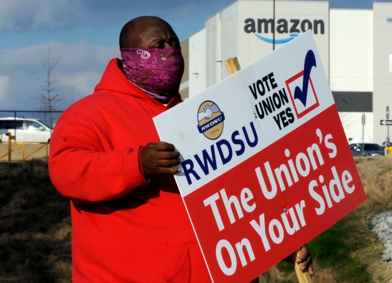 In this Tuesday, Feb. 9, 2021, file photo, Michael Foster of the Retail, Wholesale and Department Store Union holds a sign outside an Amazon facility where labor is trying to organize workers in Bessemer, Ala. 
