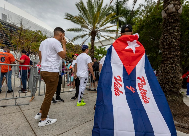 A man wearing a Cuban flag bearing the slogan of Patria y Vida walks toward the stadium before a World Baseball Classic game between between Cuba and the United States, Sunday, March 19, 2023, in Miami. 