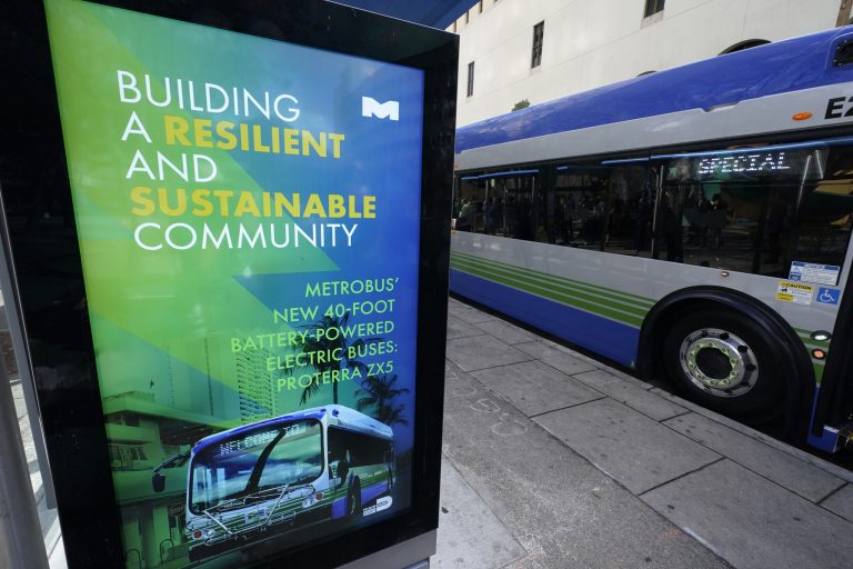 A billboard announces the benefits of Proterra ZX5 battery-powered electric buses as one is parked at a bus stop, Feb. 2, 2023, in downtown Miami. Electric bus and truck maker Proterra says it is seeking Chapter 11 bankruptcy protection from a federal court in Delaware.
