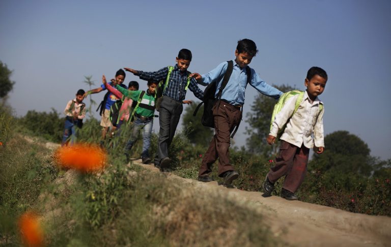 In this April 5, 2013 photo, wearing new donated shoes, impoverished children walk towards a free school run under a mass transit bridge in New Delhi, India. (AP Photo/Altaf Qadri)
