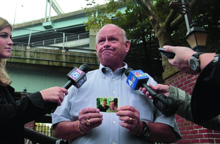 Ken Fairben holds a photo showing his son Keith, left, a victim of the Sept, 11, 2001 attacks, as he holds a press briefing on Monday, Oct. 15, 2012, outside Fort Hamilton Army base in Brooklyn, N.Y. Military installations in New York, New Jersey, Massachusetts and Maryland are welcoming families of 9/11 victims this week to watch pretrial hearings in Cuba for five men charged in the terrorist attacks via closed-circuit television. (AP Photo/Bebeto Matthews)