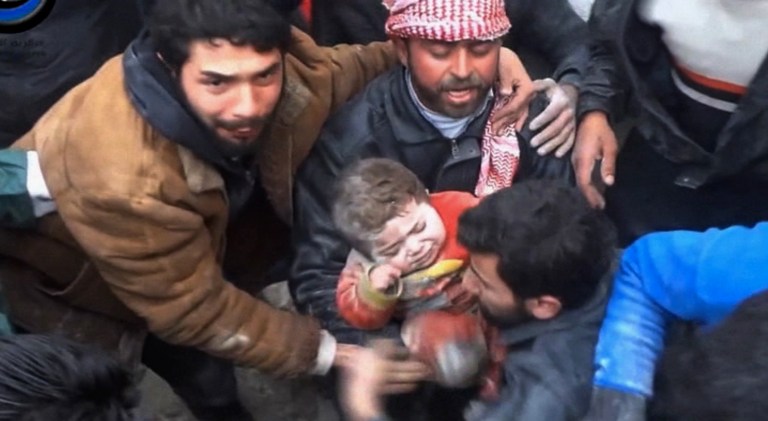 In this citizen journalism image made from Wednesday, Jan. 22, 2014 video provided by Nur Media Center, an anti-government activist group, which has been authenticated based on its contents and other AP reporting, one of the men holds 14-month-old Ghina Khalil after they dig her out of rubble in Aleppo, Syria. The chubby toddler was pulled out after men pulled aside rocks, concrete rubble and dust to free her, caught under a smashed building, bombed by the government forces in the area of Masaraniyeh in Aleppo. (AP Photo/Nour Media Center)