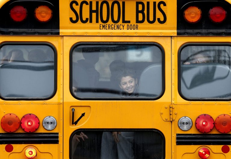   A returning student smiles as his bus school bus pulls into Hawley School, Tuesday, Dec. 18, 2012, in Newtown, Conn. Classes resume Tuesday for Newtown schools except those at Sandy Hook. Buses ferrying students to schools were festooned with large green and white ribbons on the front grills, the colors of Sandy Hook. At Newtown High School, students in sweatshirts and jackets, many wearing headphones, betrayed mixed emotions. Adam Lanza walked into Sandy Hook Elementary School in Newtown, Friday and opened fire, killing 26 people, including 20 children, before killing himself.(AP Photo/Jason DeCrow)  