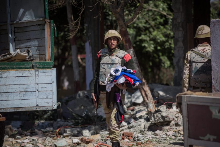 An Egyptian military police soldier carries clothes found on the ground of a checkpoint attacked by gunmen in Shubra al-Kheima, a suburb north of Cairo, Egypt, Saturday, March 15, 2014. Egypt's state news agency said gunmen attacked a checkpoint manned by the military police in the suburb on early Saturday, killing several of them. (AP Photo/Eman Helal)