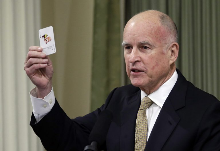 Gov. Jerry Brown displays a playing card with his dog, Sutter, on it as he gives the annual State of the State speech before a joint session of the Legislature at the Capitol in Sacramento, Calif., Wednesday, Jan. 22, 2014.  Brown delivered a dual message in his annual address to the Legislature, that a California resurgence is well underway but is threatened by economic and environmental uncertainties.  On the backside of the playing card is a chart showing how high deficits follow balanced budgets, and warned that even though there is a budget surplus, lawmakers should not overspend.(AP Photo/Rich Pedroncelli)