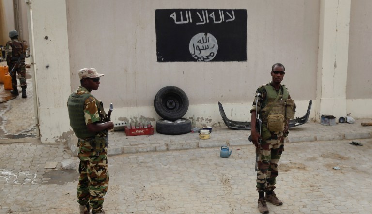 Chadian soldiers stand at a checkpoint in front of a Boko Haram flag the Nigerian city of Damasak, Nigeria, Wednesday March 18, 2015. Damasak was flushed of Boko Haram militants last week, and is now controlled by a joint Chadian and Nigerien force.