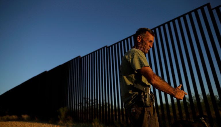 In this May 10, 2016, picture, an armed border security volunteer gestures as he stands along the border wall separating Mexico and the United States in Sasabe, Ariz.
