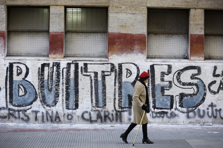 A woman walks by a graffiti that reads in Spanish 