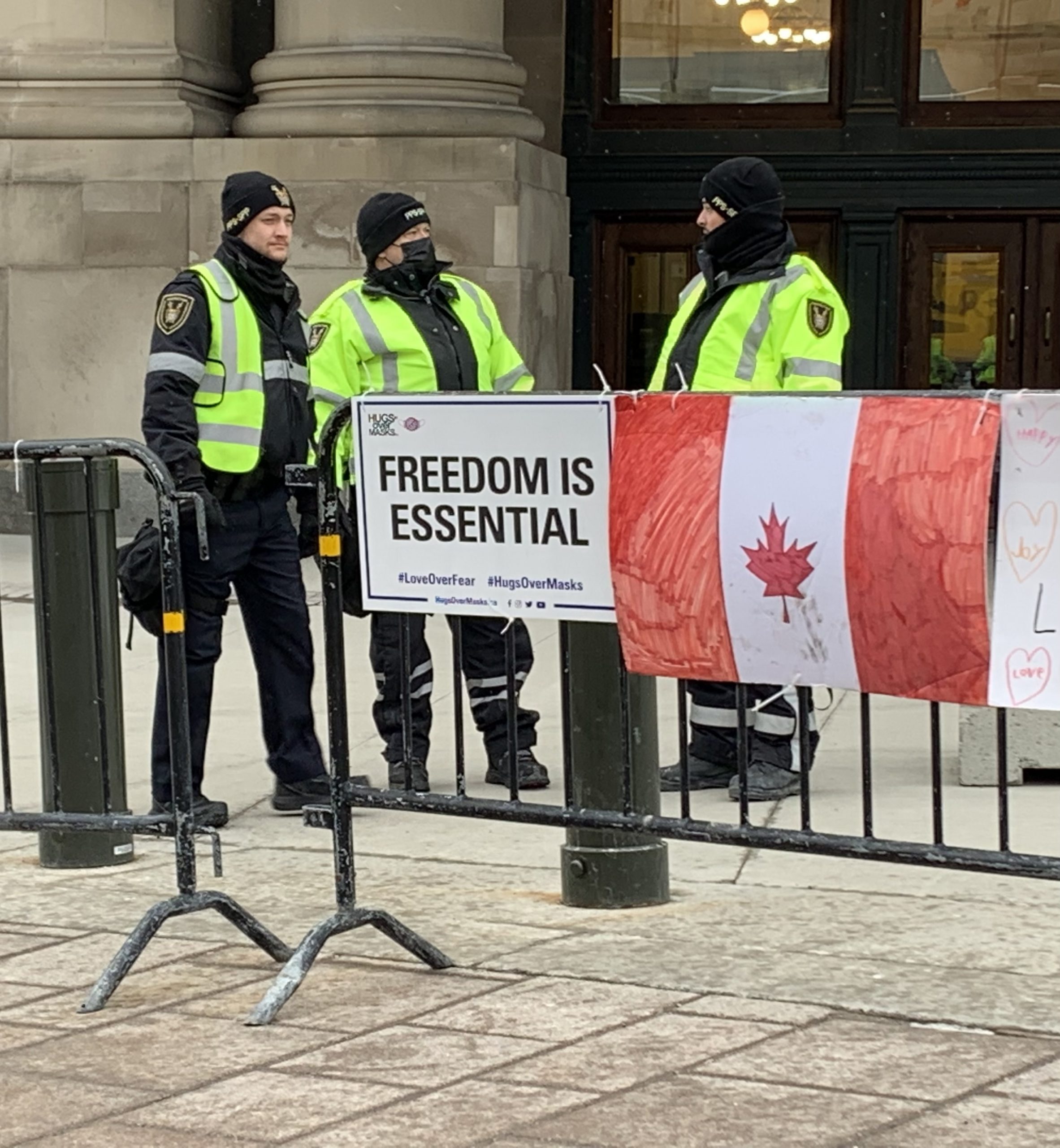 Canadian police officers stand outside a government building in Ottawa, Ontario. A sign nearby reads, "Freedom is essential."