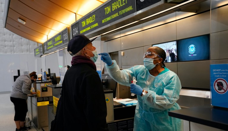 Licensed vocational nurse Caren Williams, left, collects a nasal swab sample from a traveler at a COVID-19 testing site at the Los Angeles International Airport in Los Angeles, Monday, Nov. 23, 2020. 