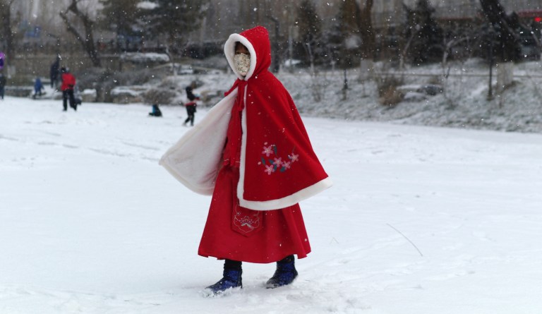 A girl wears a face mask as she walks across a frozen canal during a snowfall in Beijing, Wednesday, Feb. 5, 2020. 